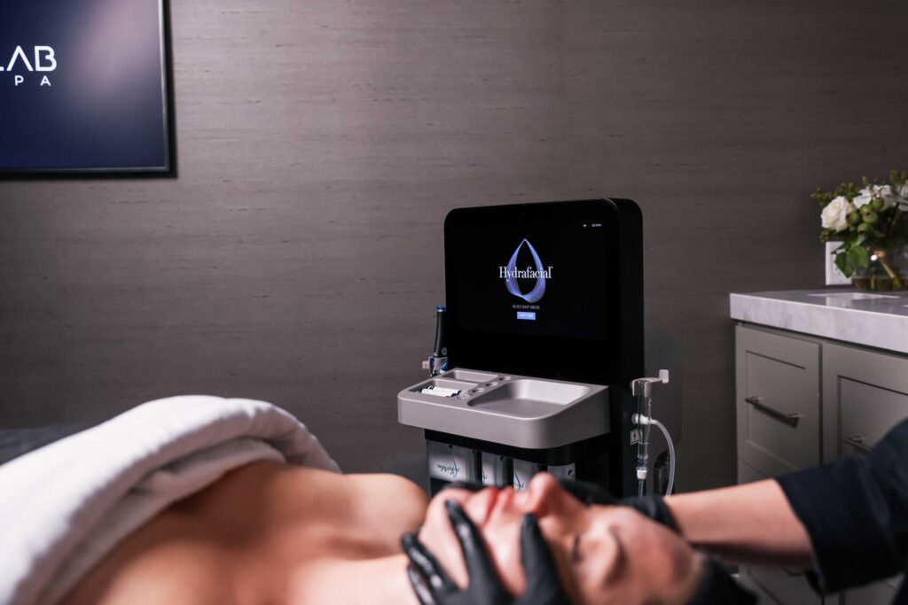 A patient relaxes on a treatment table in the foreground as the latest Syndeo technology glows in the background. This next-gen tech is part of the reason Look Lab delivers the best Hydrafacial in Denver.